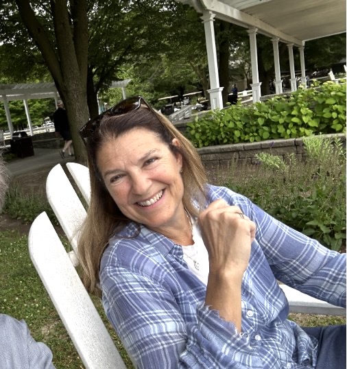 Tracy Granzyk smiling, seated in a white Adirondack chair outdoors